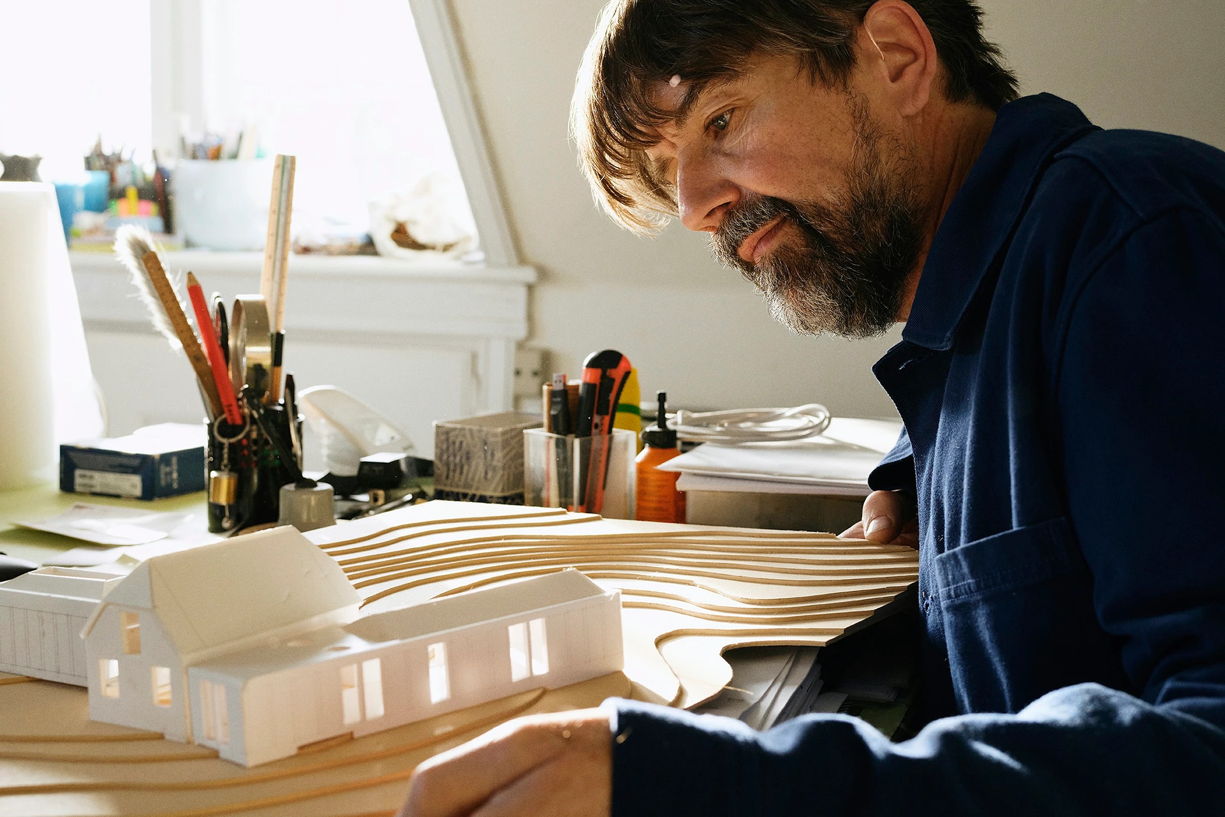 Documentary photograph of a designer refining an architectural model at a working studio desk