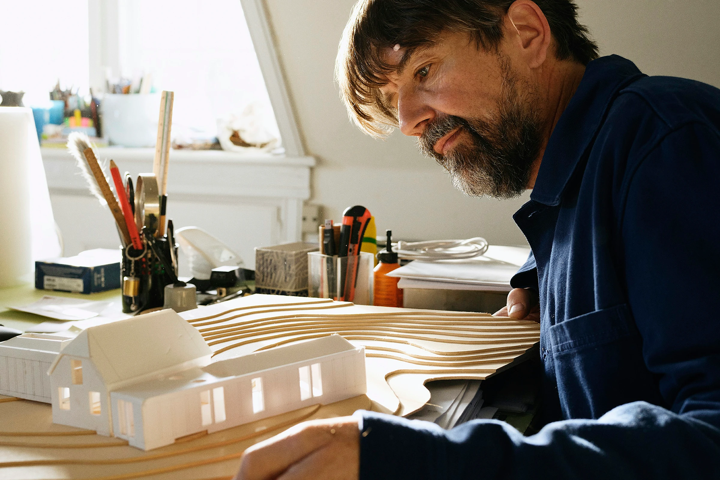 Documentary photograph of a designer refining an architectural model at a working studio desk